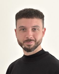 Foto zeigt ein Porträt von Möbeldesigner und Industriedesigner Felix Angermeyer aus Köln. Er trägt ein schwarzes Oberteil, dunkle Locken und einen Bart. Er lächelt direkt in die Kamera. Das Foto wurde von Felix selbst aufgenommen.